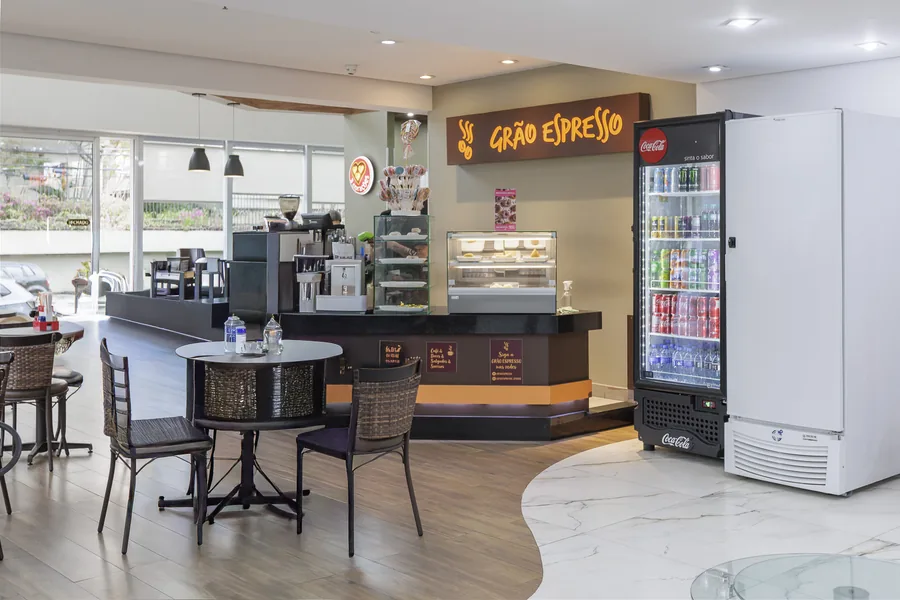 Cafeteria Grão Espresso no térreo do prédio, com balcão, mesas e vitrine de doces